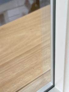 Close-up of a clean, clear window with vacuum glazing, showcasing its advanced insulation. Outside, a wooden deck is visible. The image captures the edge of the window pane and part of the white window frame.