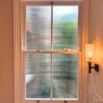 Reeded glass sash window in a bathroom, providing privacy while allowing natural light through timber joinery.