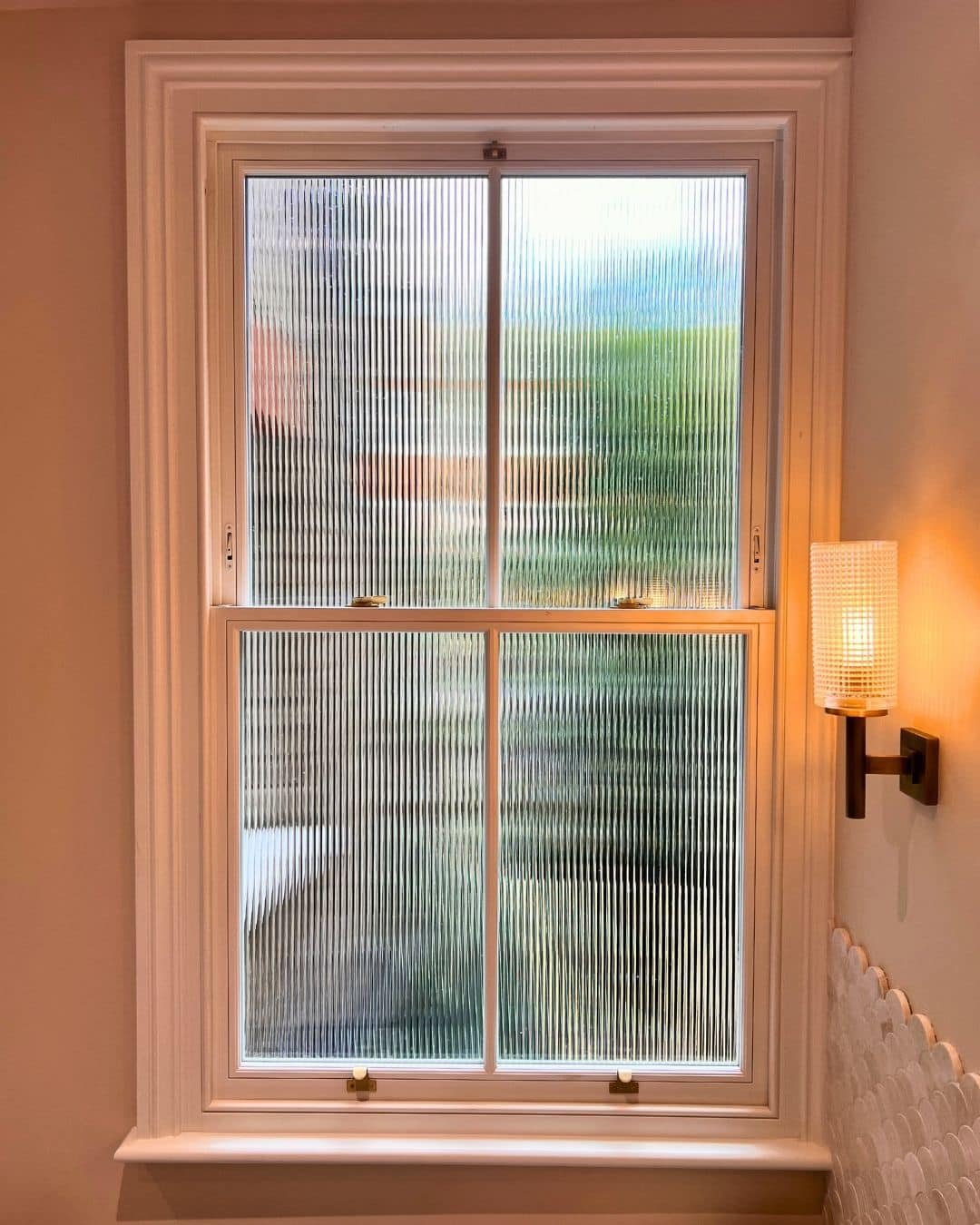 Reeded glass sash window in a bathroom, providing privacy while allowing natural light through timber joinery.